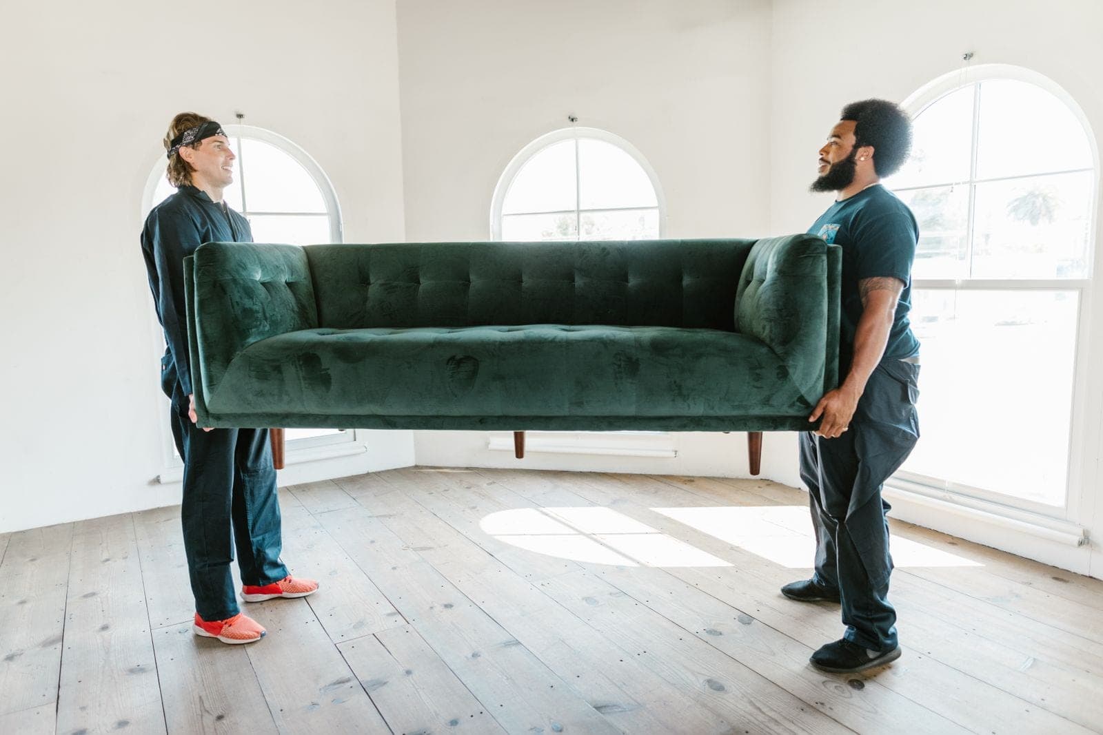 Two movers lifting a green sofa in an empty room
