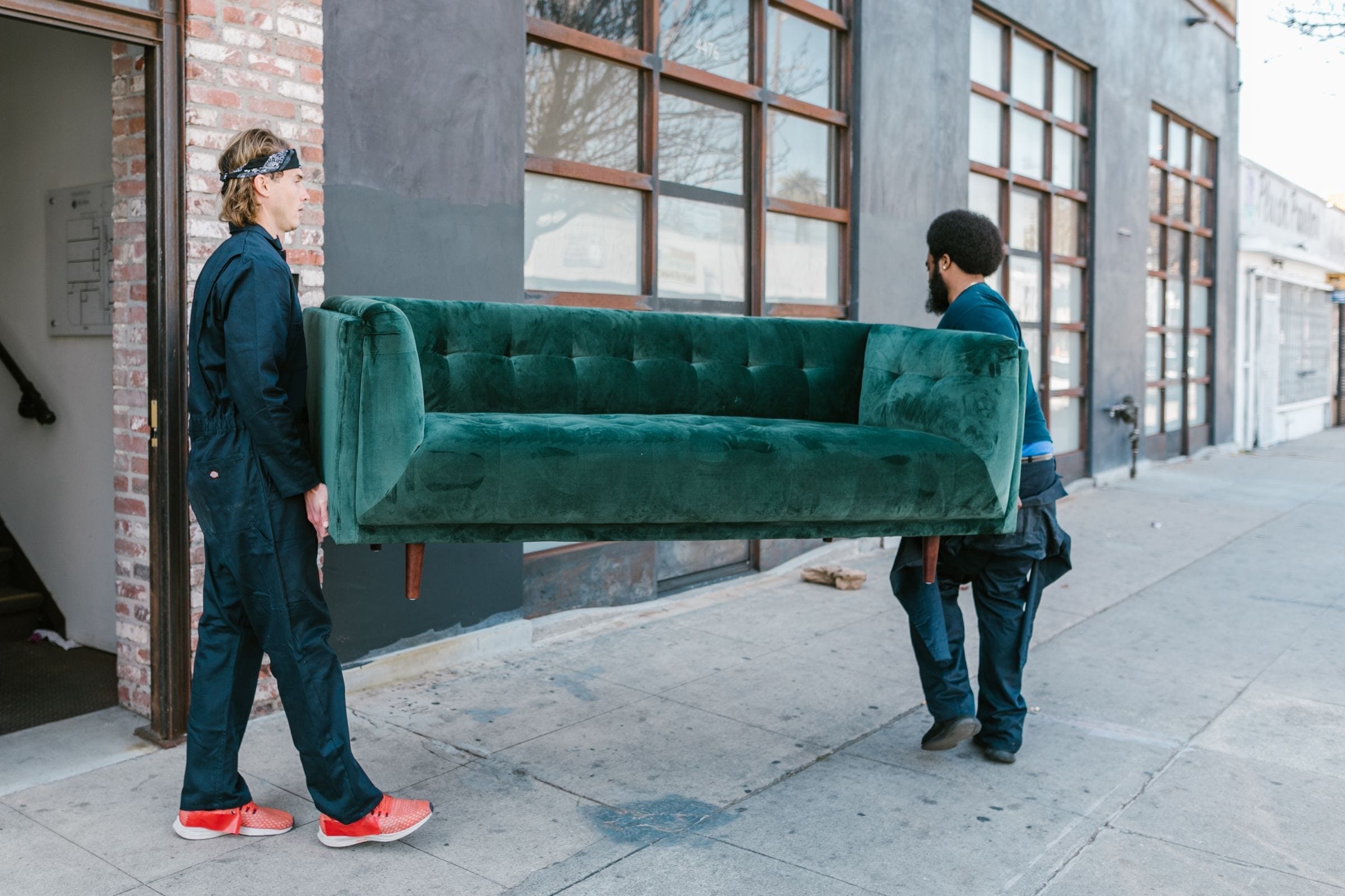 Two movers carrying a green sofa along a sidewalk, a typical junk removal job in Moncton