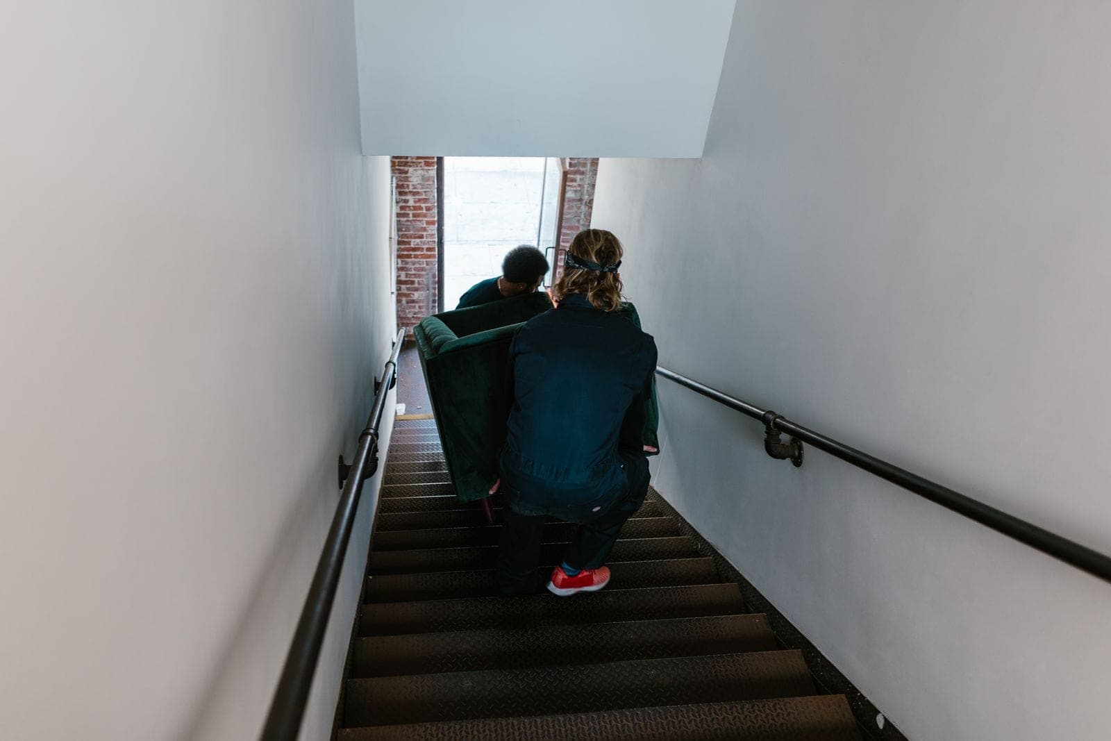 Two movers carrying a couch up a narrow stairwell